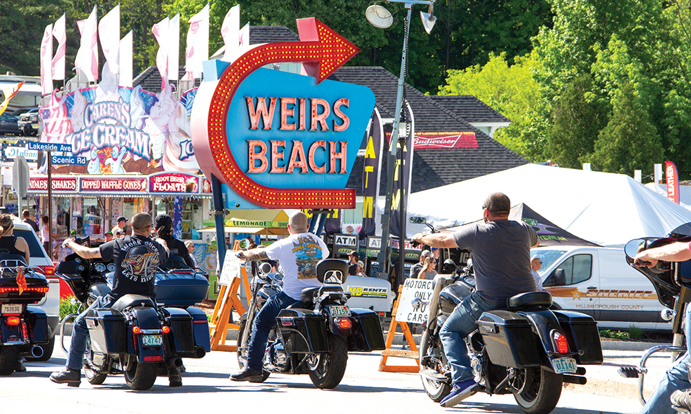 Bikers drive past Weirs Beach entrance sign during Bike Week